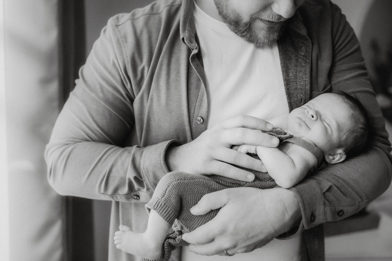 A new dad holding his newborn baby in his arms illuminated by window light captured by a Winchester Virginia Newborn photographer