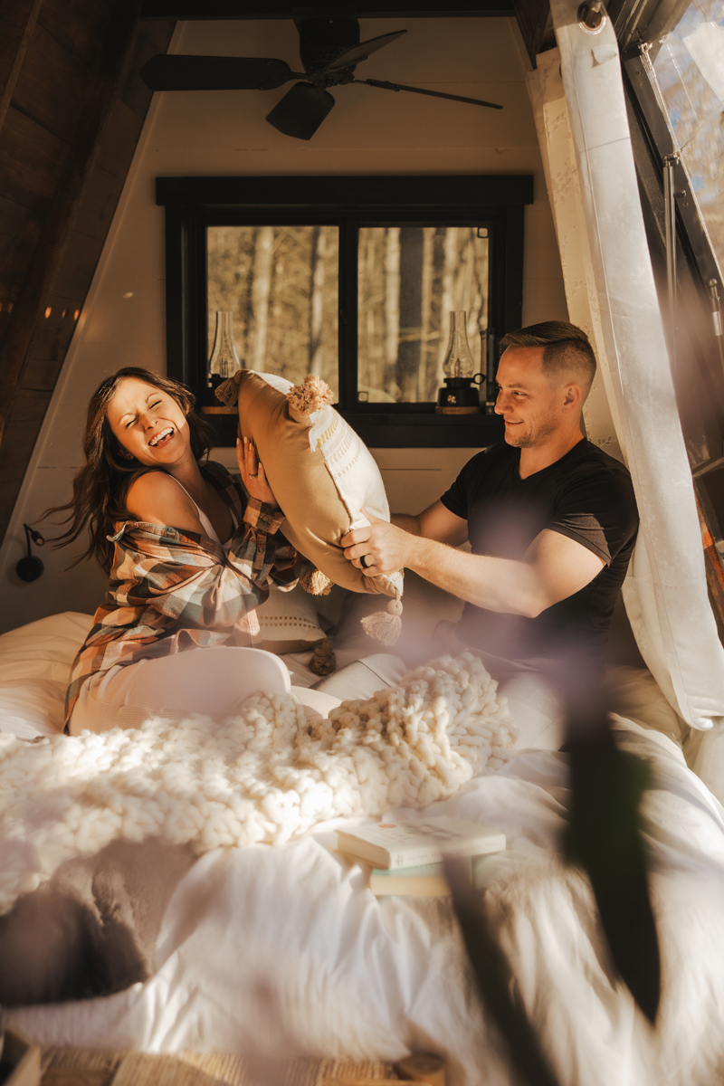 A couple having a playful pillow fight in a light filled cabin captured by a Cumberland Maryland Elopement photographer