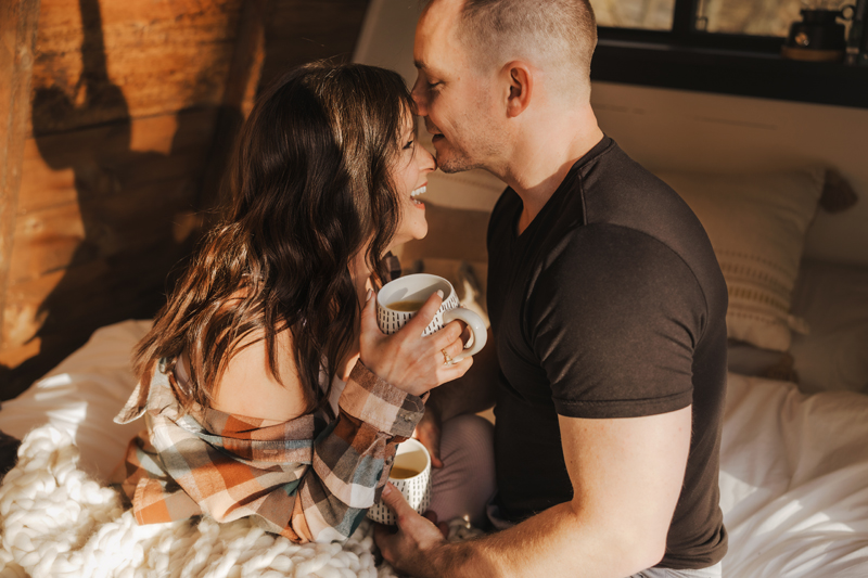 a couple lovingly sharing coffee and laughing together in a cozy cabin captured by a Winchester Virginia couples photographer